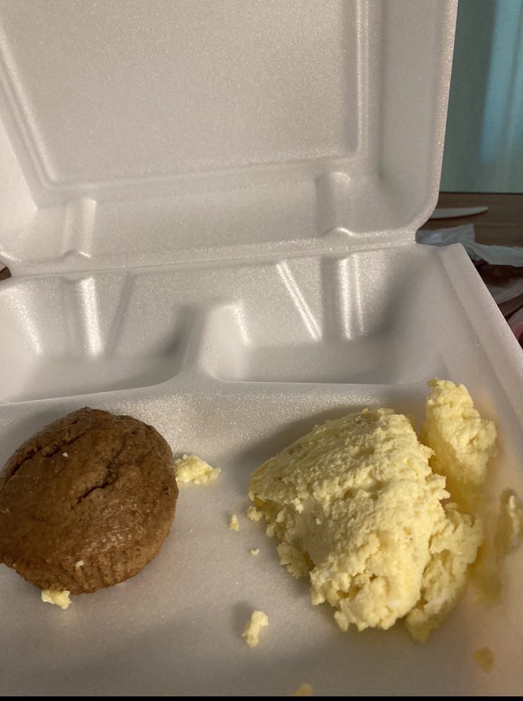 A takeout container with a muffin and scrambled eggs.