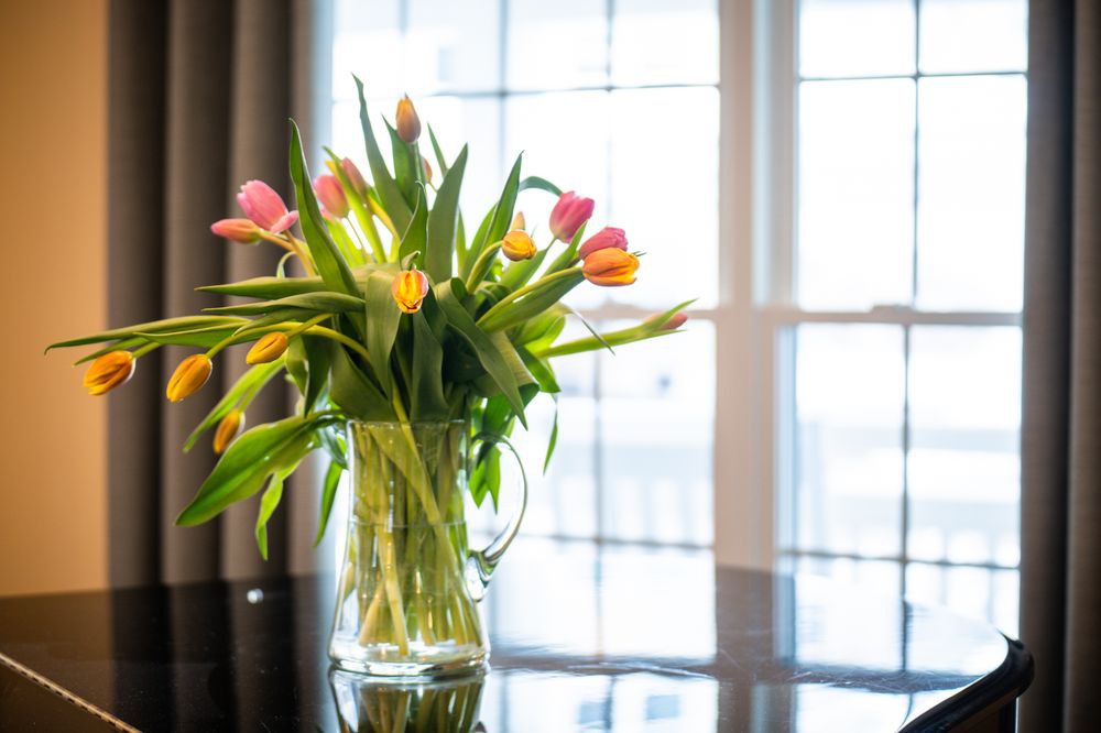 A vibrant bouquet of tulips in a vase on a reflective surface, illuminated by natural light.