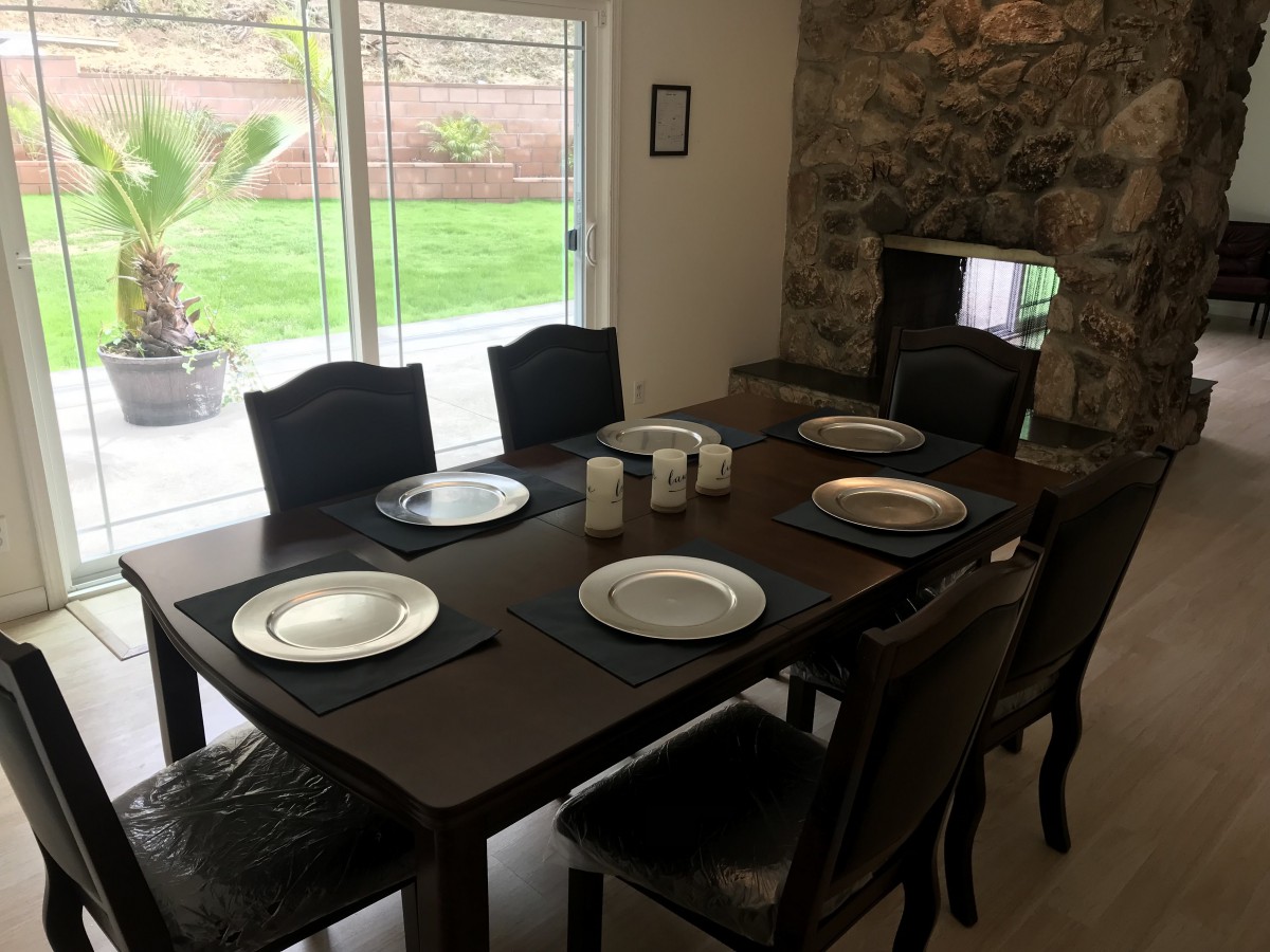 A dining table set for six with plates and candles, overlooking a garden through a large window.