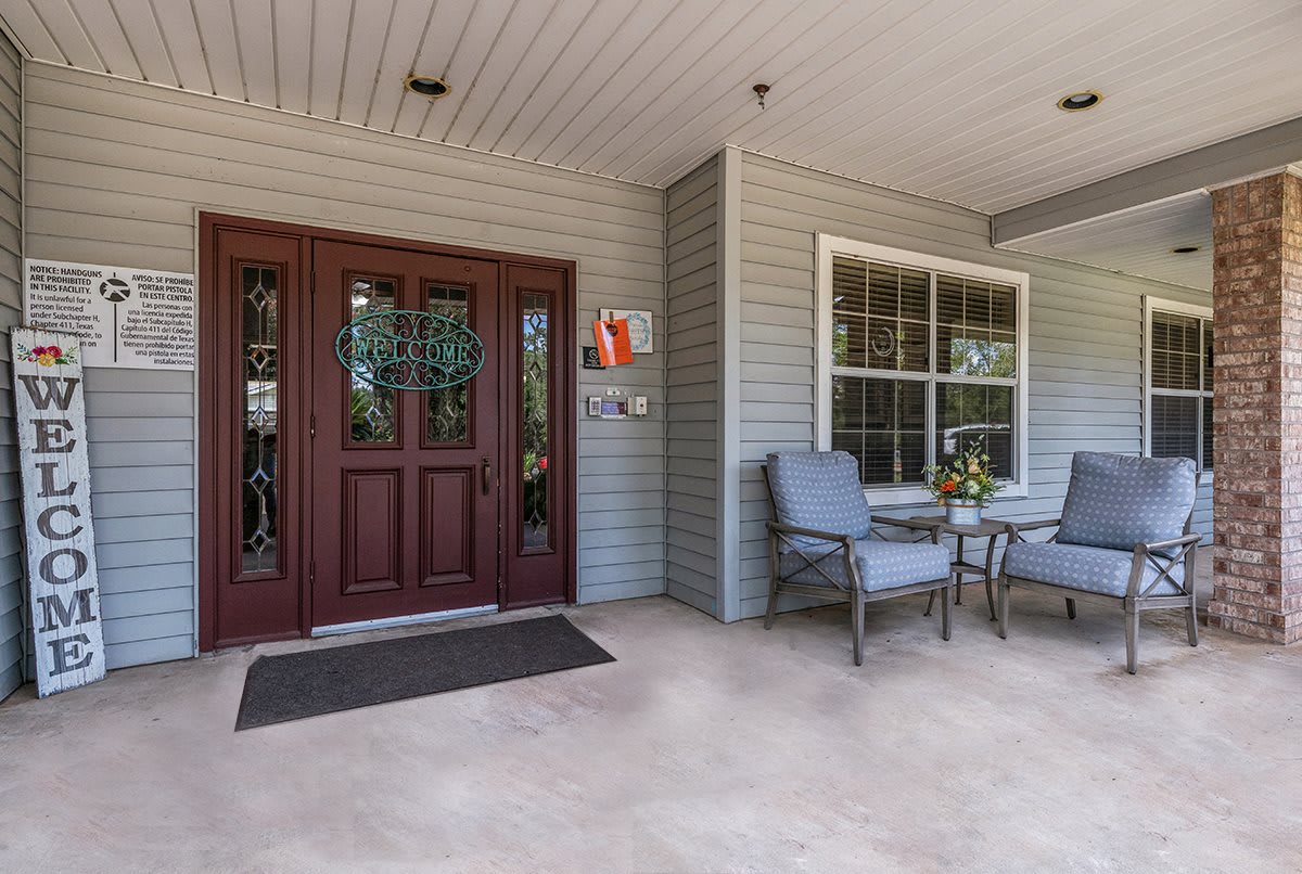 A cozy front porch with armchairs and a small table next to a wooden entrance door.