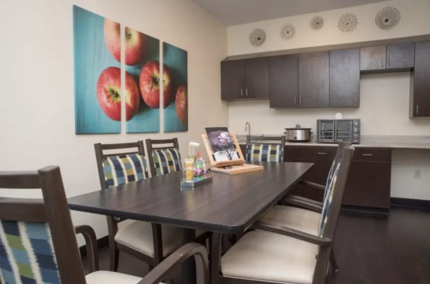 A modern dining area with a dark wooden table, cushioned chairs, and vibrant tomato wall art.