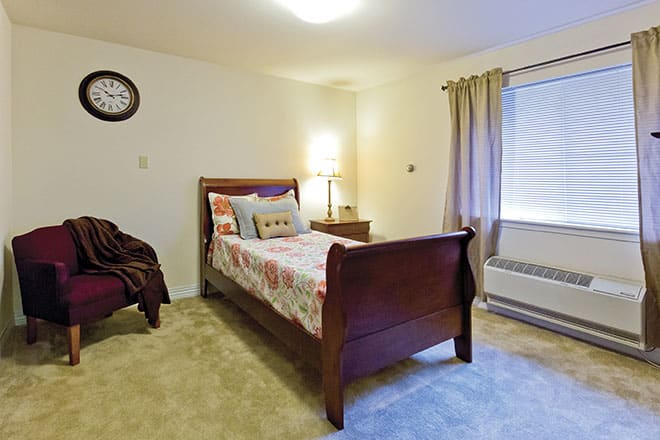 A cozy bedroom with a wooden bed, bedside lamp, and large window with curtains.