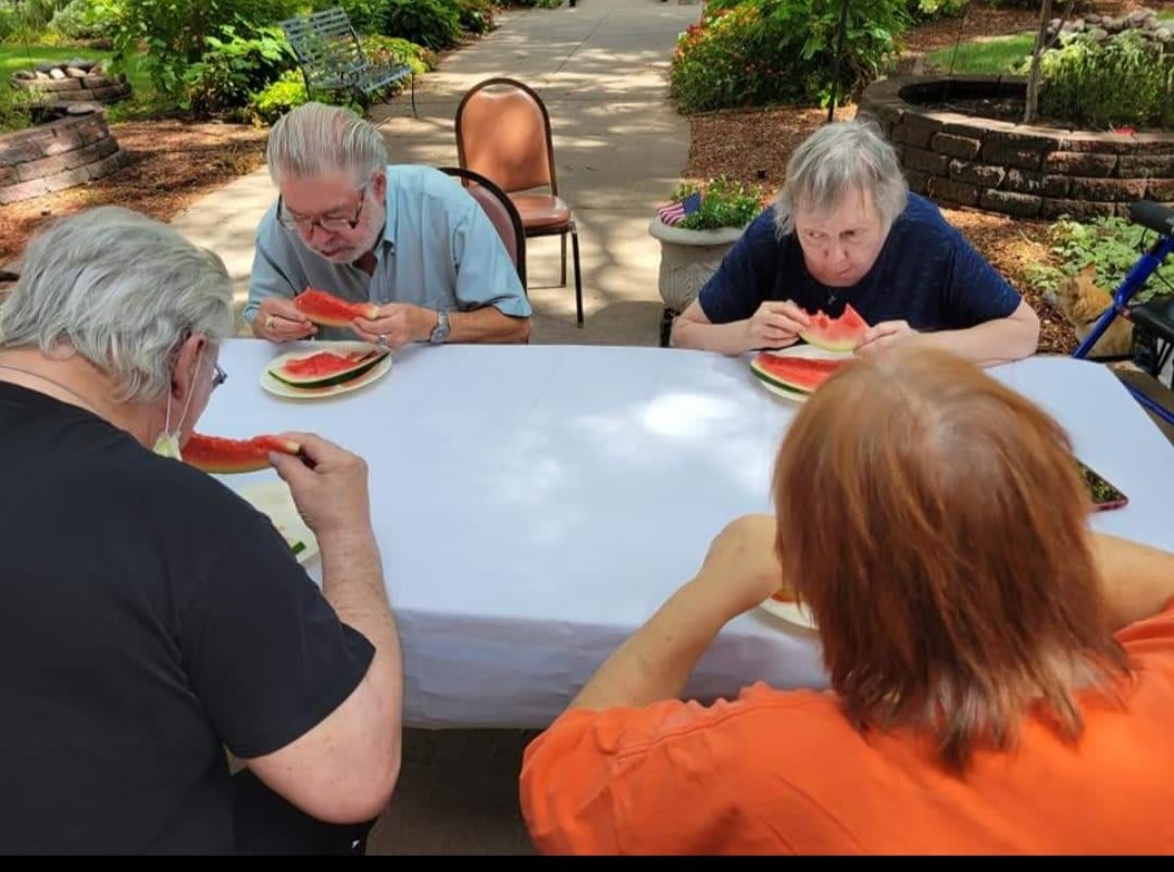 A group of people enjoying watermelon outdoors at a table in a park setting.