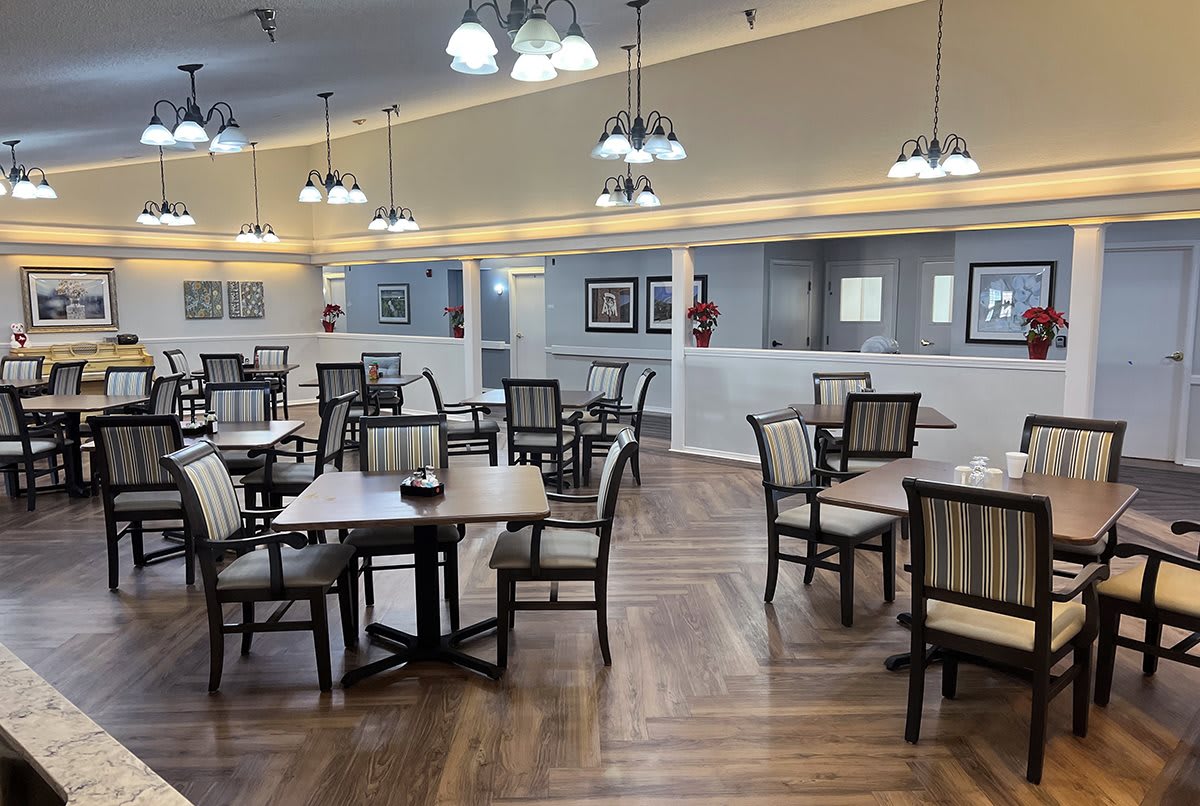 An empty dining room with wooden floors, tables, and chairs, featuring modern lighting and decor.