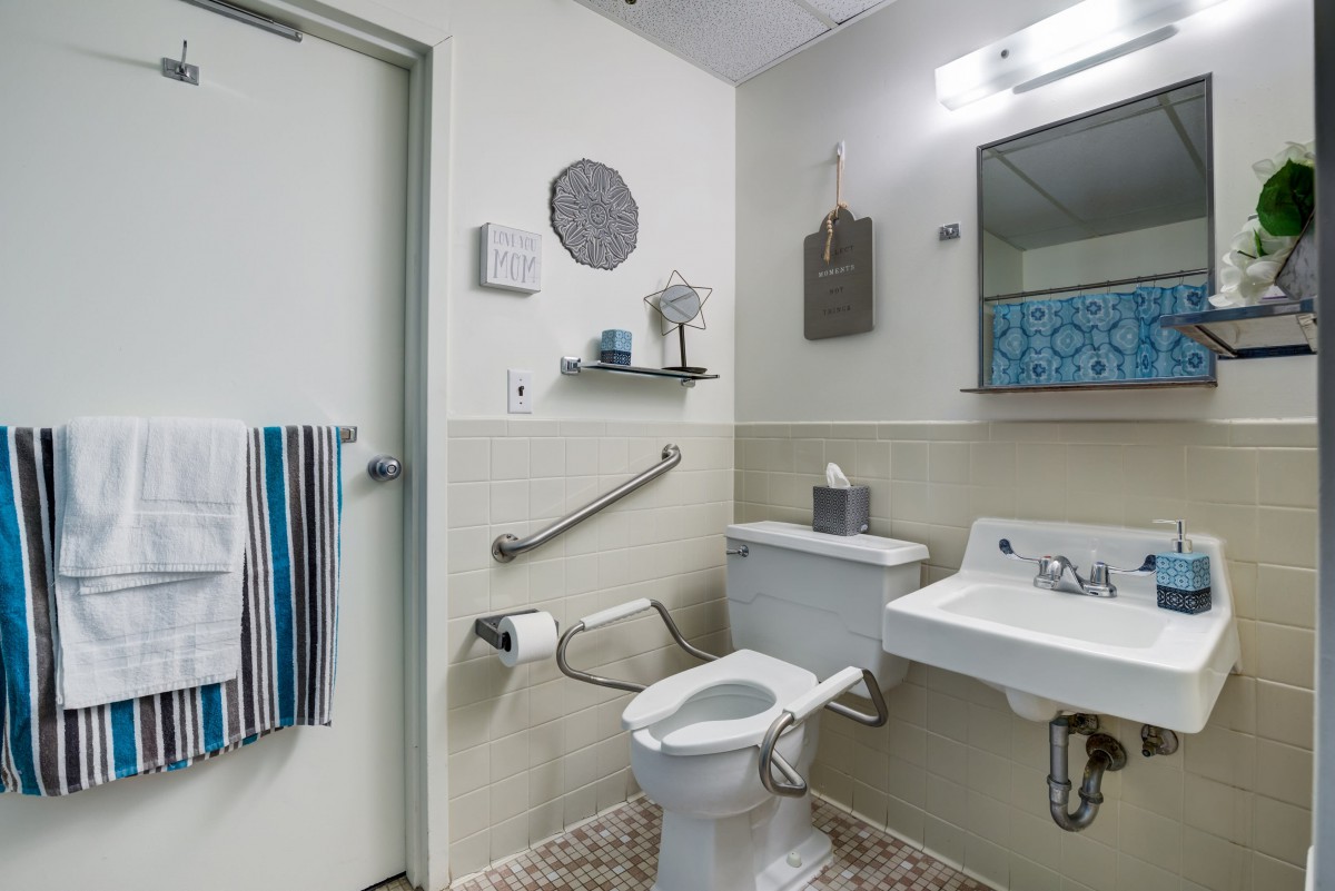 A modern bathroom equipped with a toilet, sink, mirror, and safety handrails.