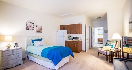A modern studio apartment interior featuring a cozy single bed and a kitchenette.