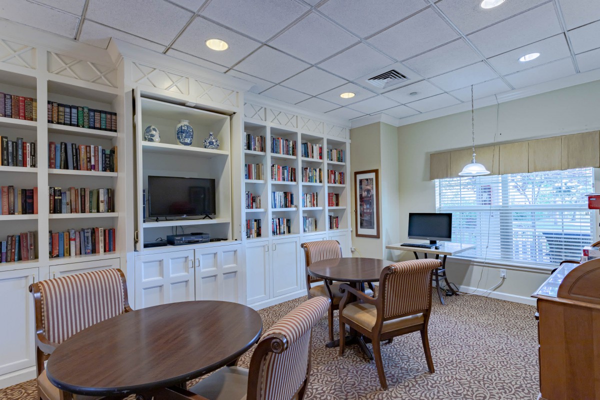 A cozy library room with bookshelves, tables, chairs, a computer station, and a television.