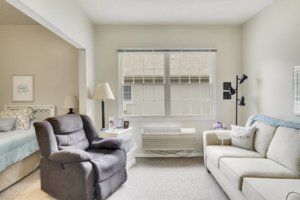 A cozy living room with a recliner, sofa, and lamps near a large window.