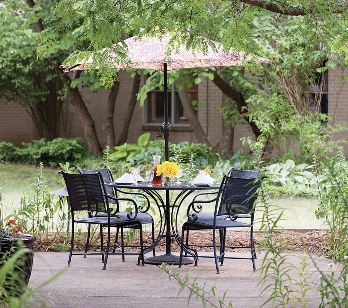 A peaceful patio setting with a table and chairs under an umbrella surrounded by lush greenery.