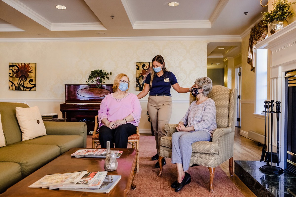 A group of seniors and a caregiver interacting in a comfortable living area.