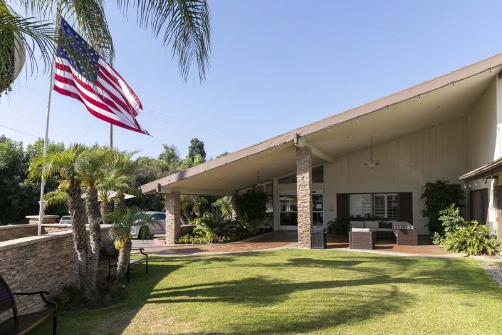 A modern house with an American flag and palm trees on a sunny day.