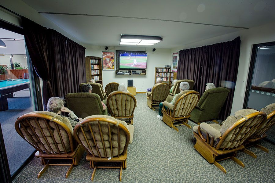A cozy living room with several chairs arranged around a TV screen, where people are gathered watching a show.