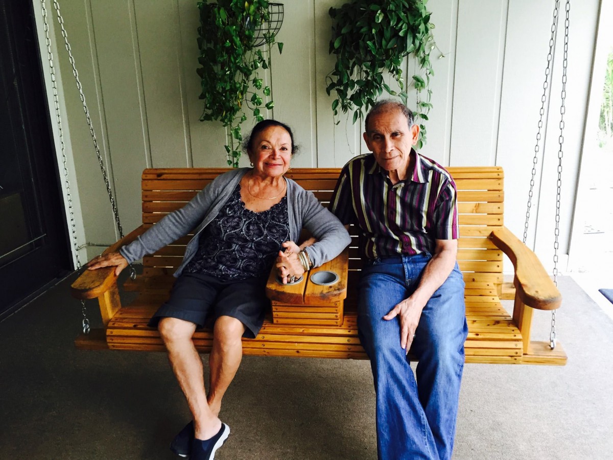 A couple sitting on a wooden bench surrounded by greenery.