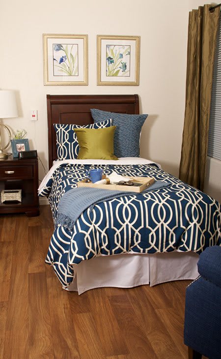 A neatly made single bed with blue geometric patterned bedding, accompanied by decorative pillows and a nightstand in a cozy bedroom setting.