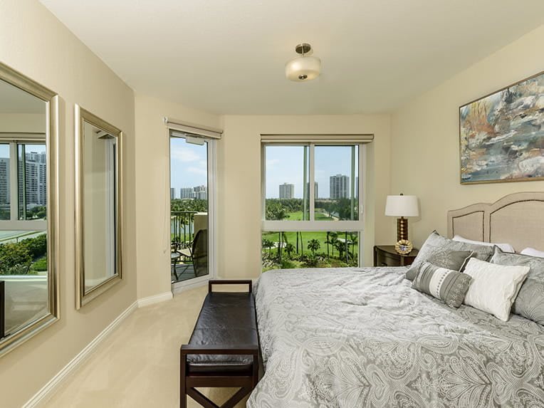 A modern bedroom featuring a large bed, neutral decor, and a view of the city through large windows.