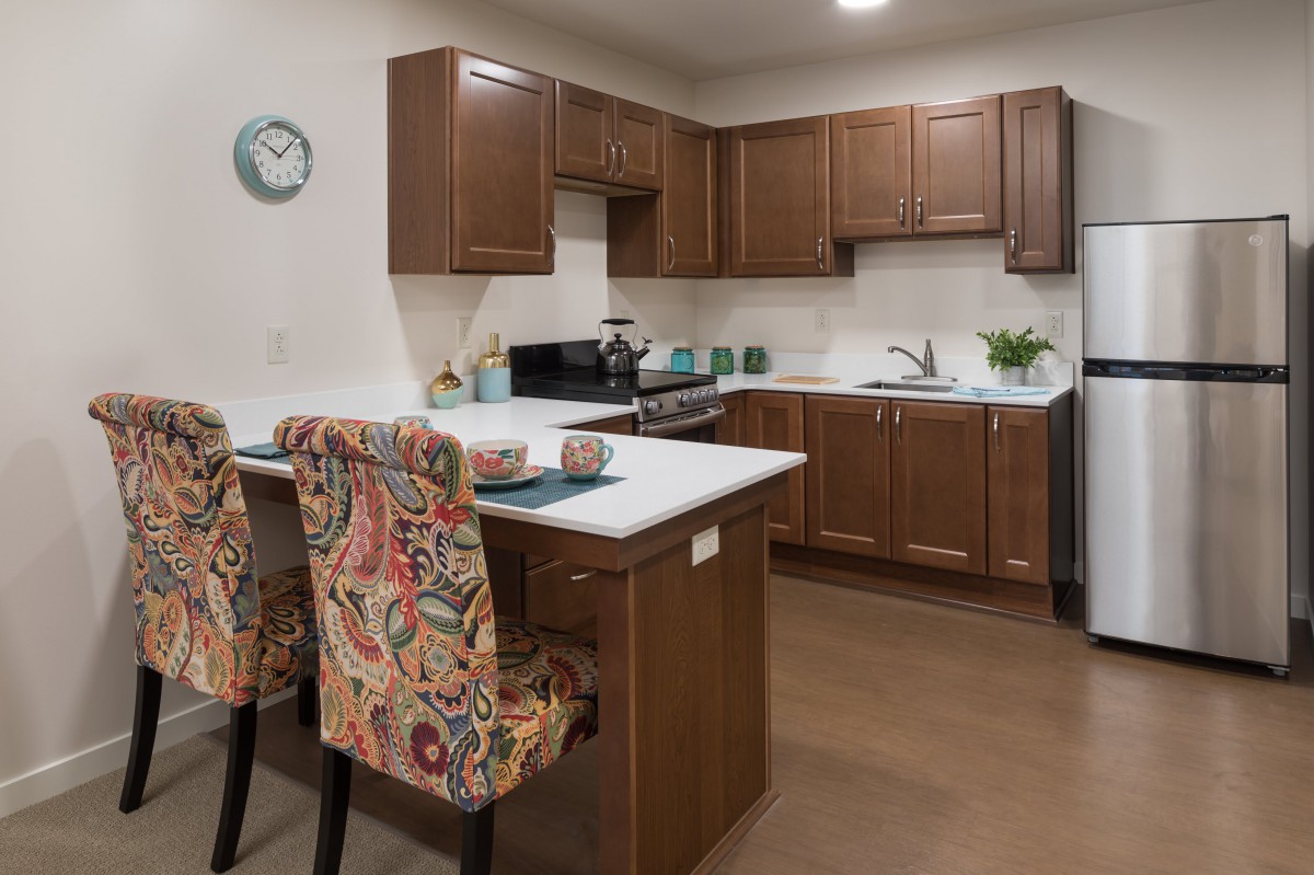 A cozy kitchen with wooden cabinets, a central island with floral upholstered chairs, and modern appliances.