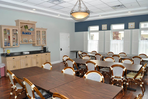 A spacious meeting room equipped with tables and chairs, featuring a kitchenette area.
