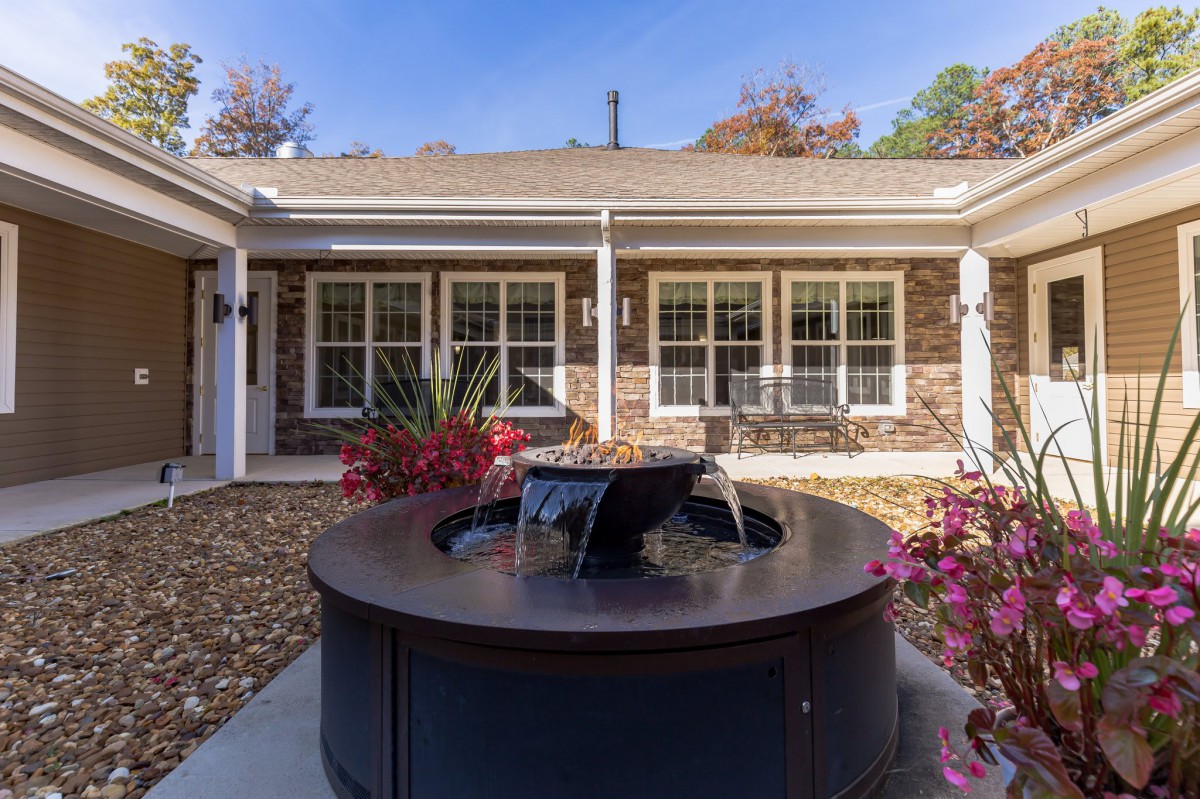 A serene courtyard featuring a central fountain surrounded by plants, with a backdrop of an elegant building facade.