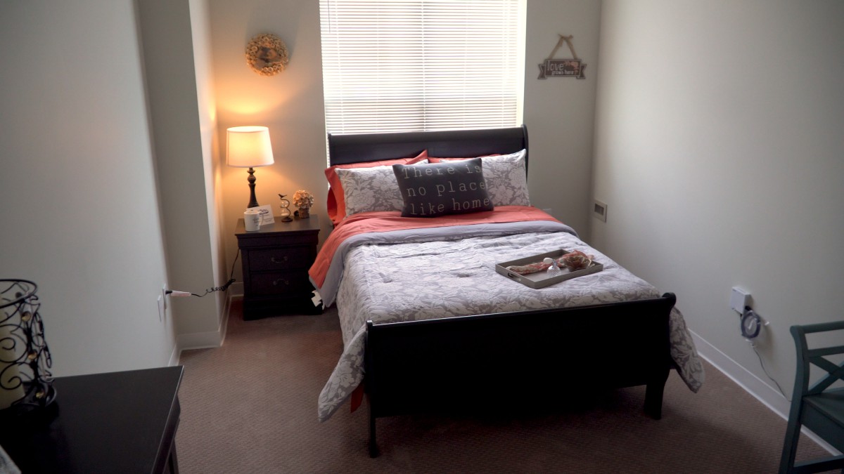 A cozy bedroom with a neatly made bed, soft lighting from a bedside lamp, and simple decor.
