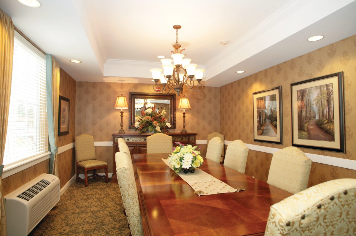 A formal dining room with elegant decor, featuring a large wooden table and upholstered chairs under a chandelier.