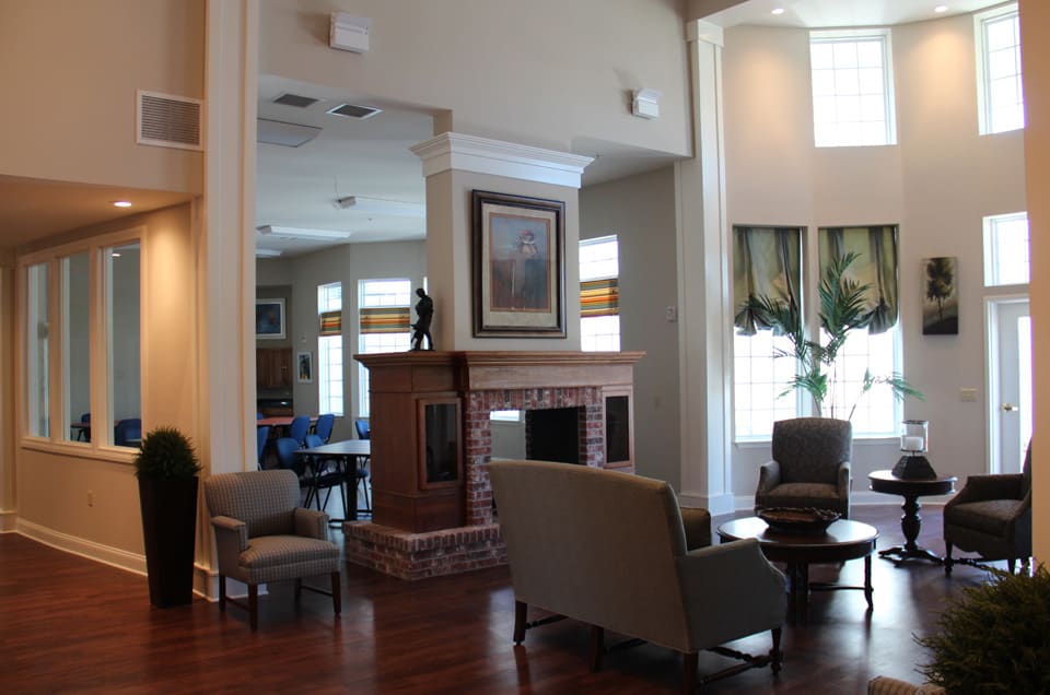 A cozy living room with a central fireplace, surrounded by comfortable seating and ample natural light from large windows.