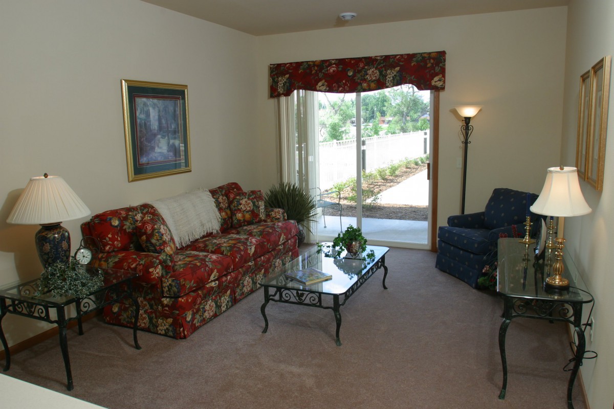 A cozy living room with a floral sofa set, glass coffee table, and sliding glass door leading to the outside.
