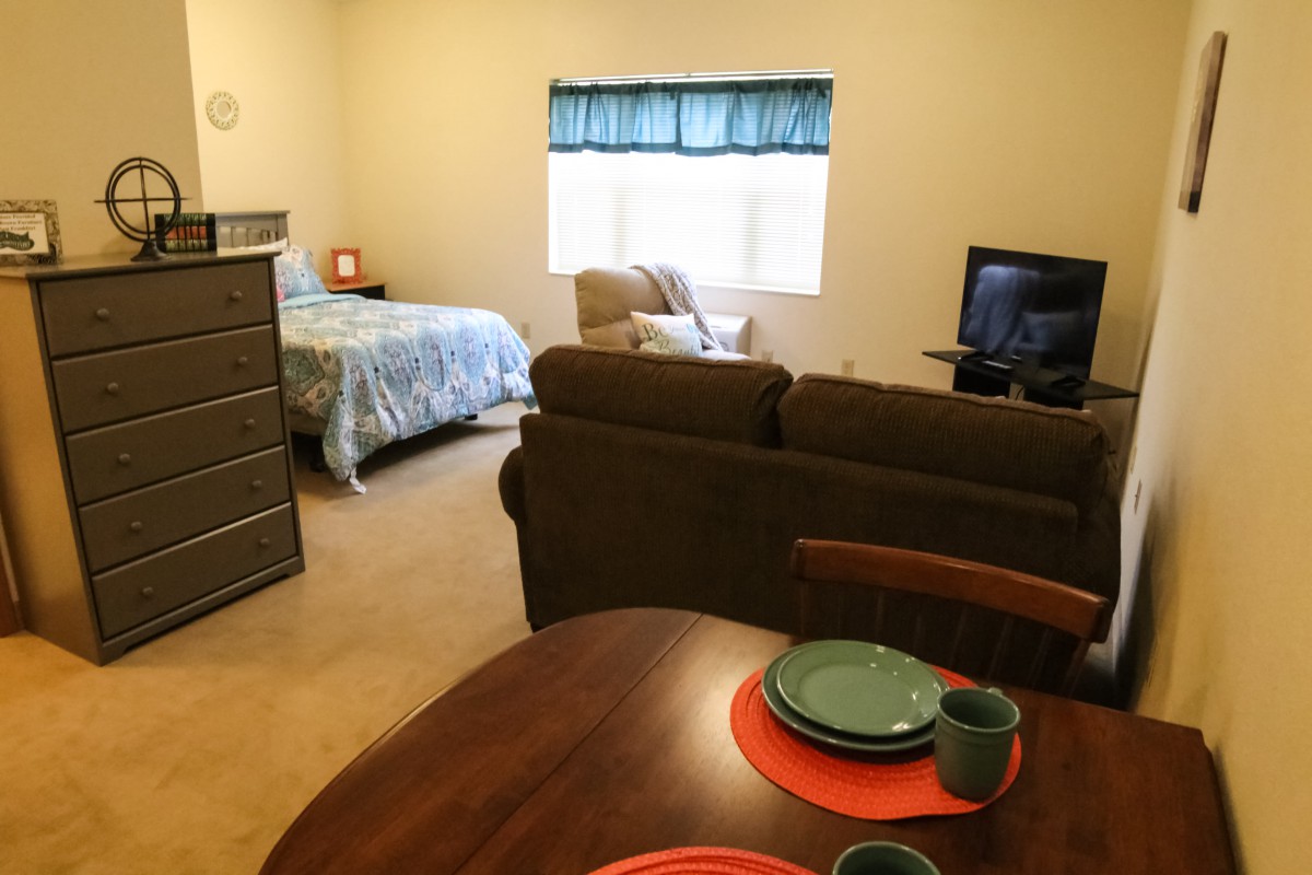 A cozy studio apartment with a bed, sitting area, and dining table.