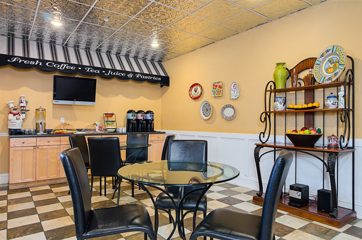 A cozy cafe interior featuring a dining area with a glass table, coffee station, and decorative plates on the wall.