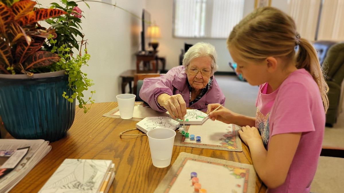 An elderly woman and a young girl engage in an art activity together at a table.
