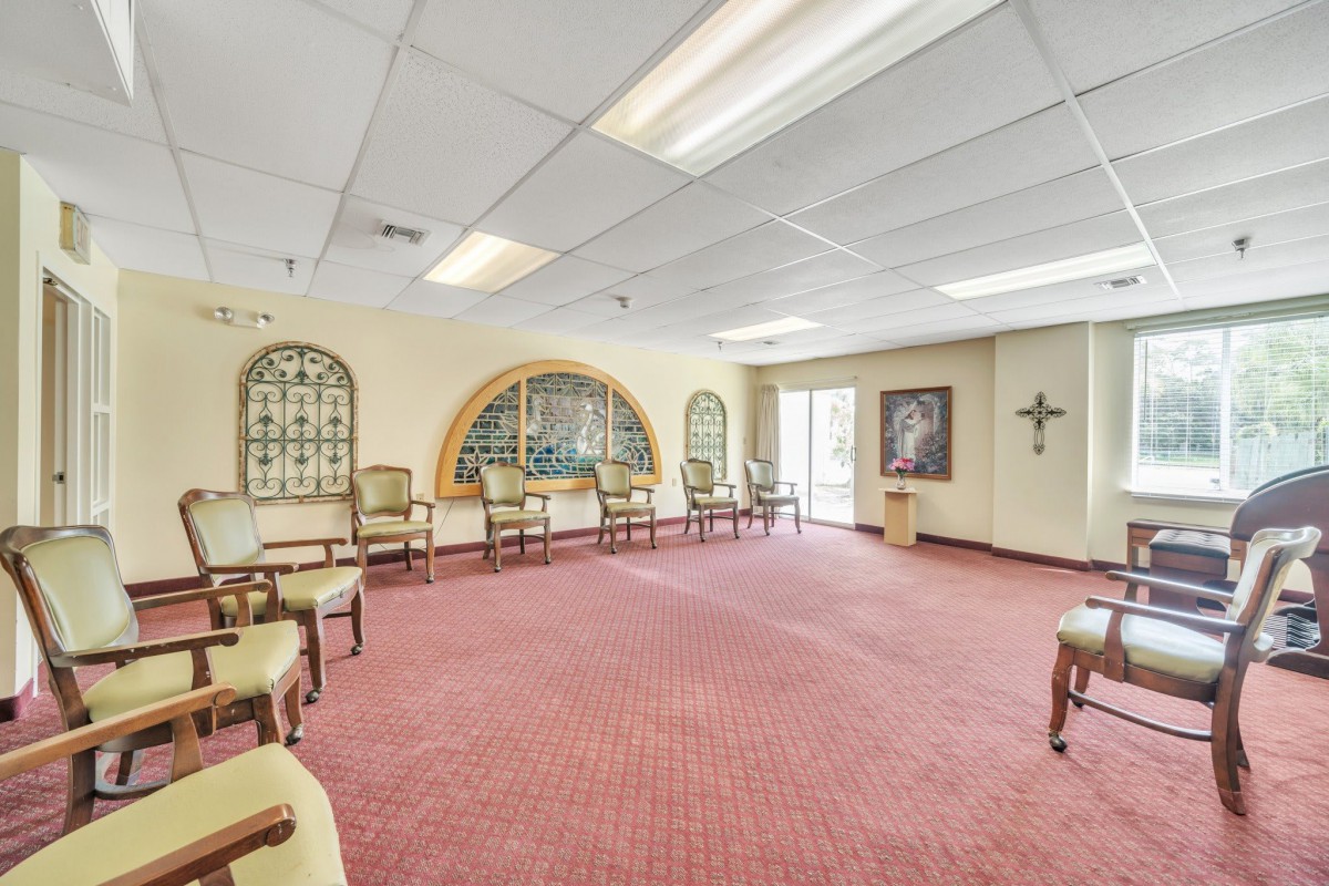 A spacious interior with multiple chairs arranged along the walls, decorative mirrors, and artwork on a carpeted floor.