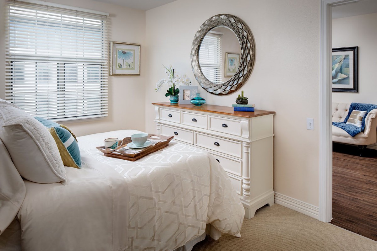 A cozy bedroom interior with a white dresser and decorative mirror.
