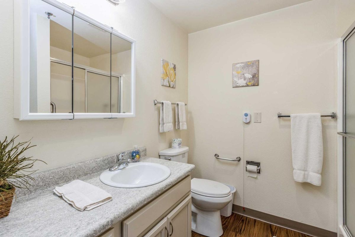 A clean, well-lit bathroom with a sink, toilet, and mirror.