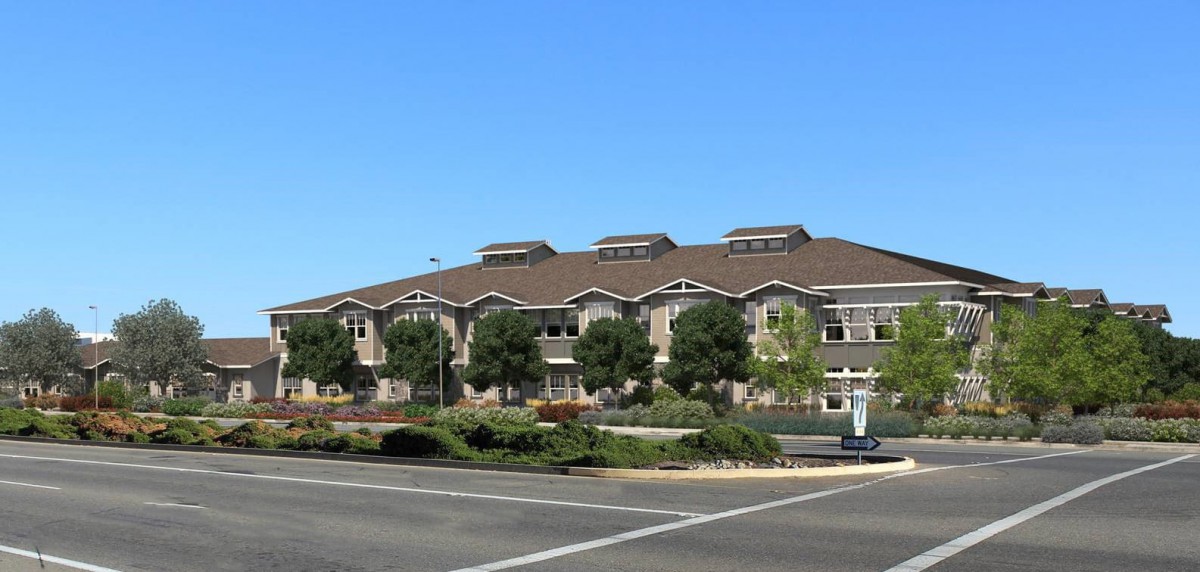 A modern building with a landscaped exterior and adjacent road under a clear blue sky.
