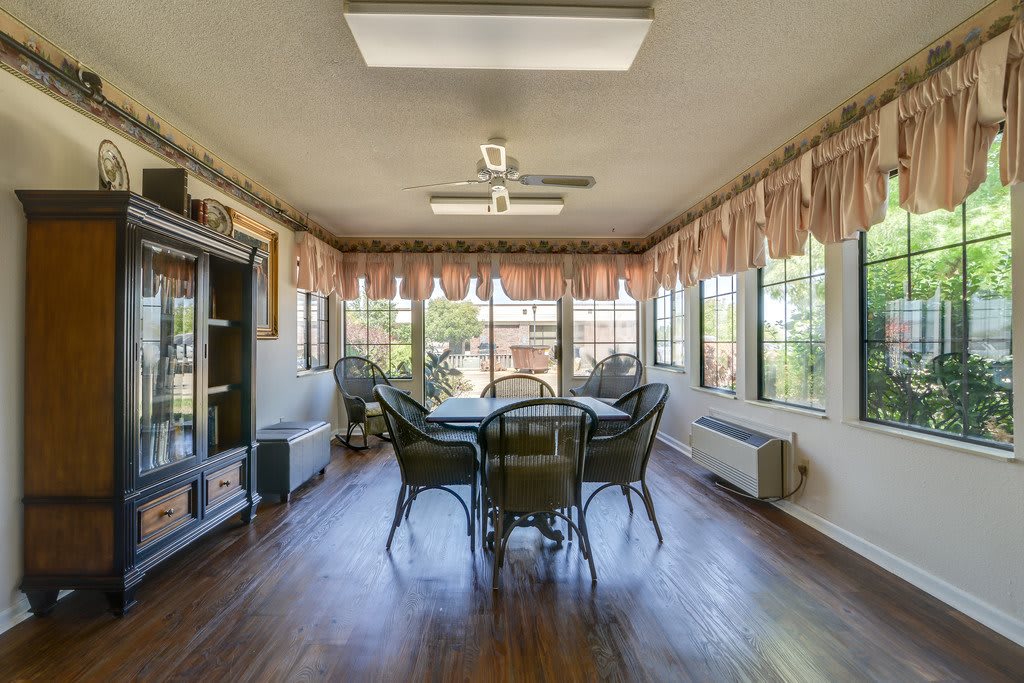A bright sunroom featuring a dining set, wicker chairs, and large windows allowing ample natural light.