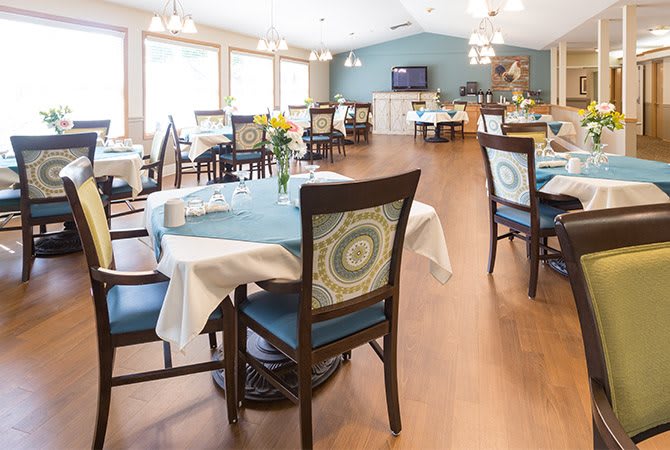 A well-lit dining area with elegantly set tables and chairs, featuring wooden flooring and modern decor.