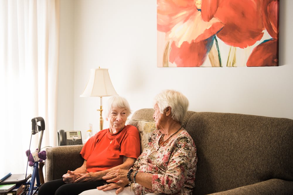 Two elderly women sitting on a sofa, engaged in conversation.