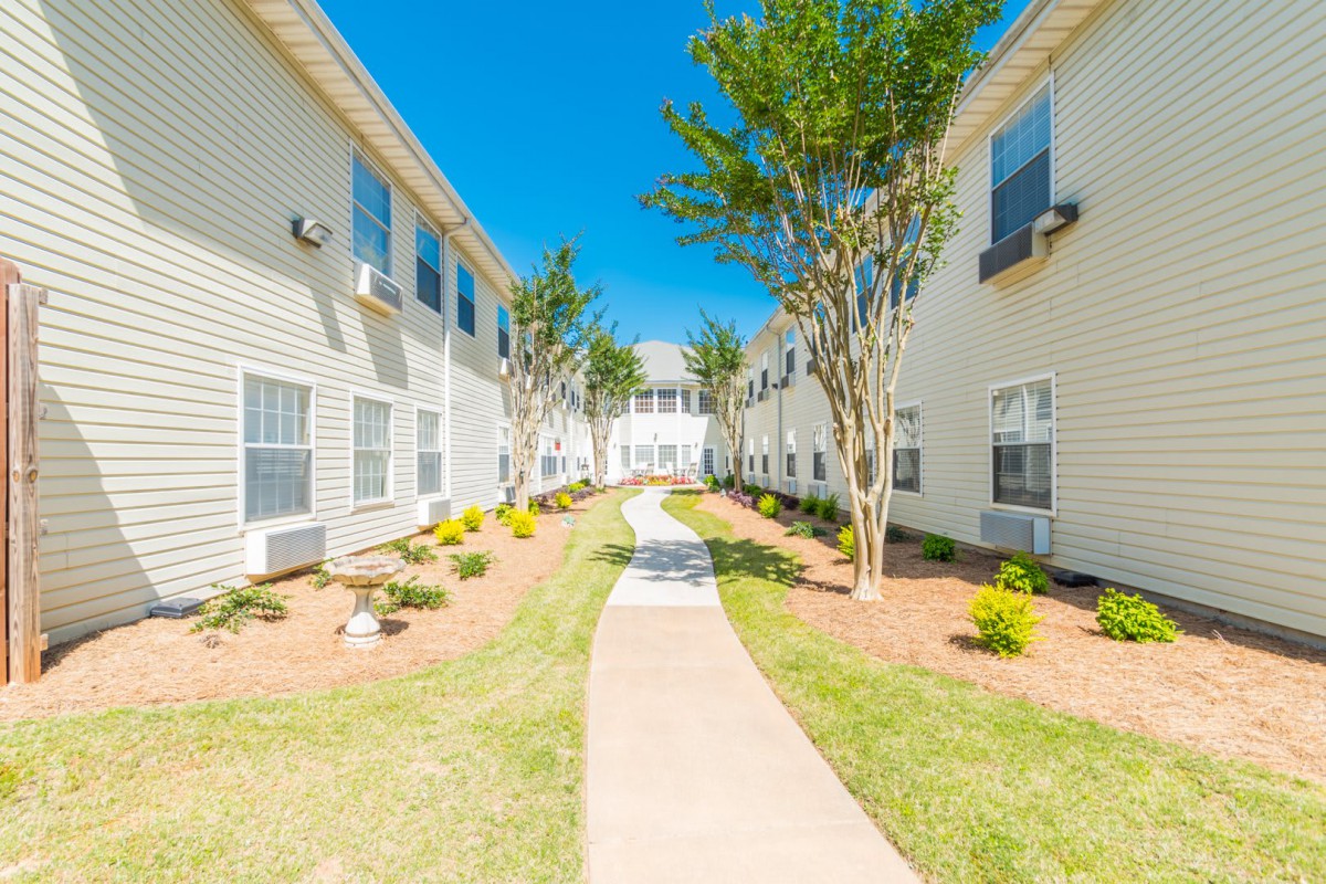 A sunny pathway between two residential apartment buildings with well-maintained landscaping.