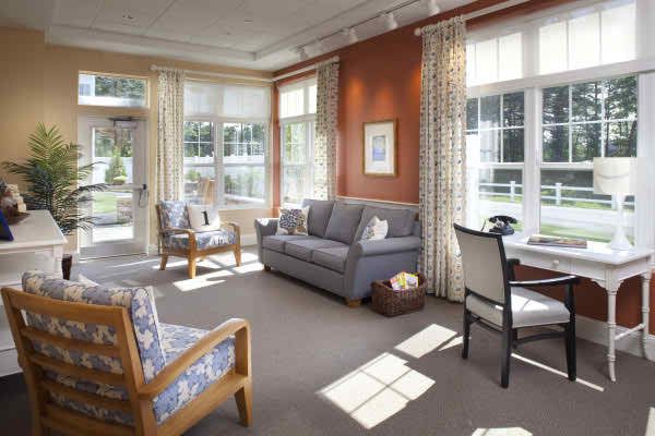 A cozy living room with a sofa, chairs, and large windows letting in natural sunlight.