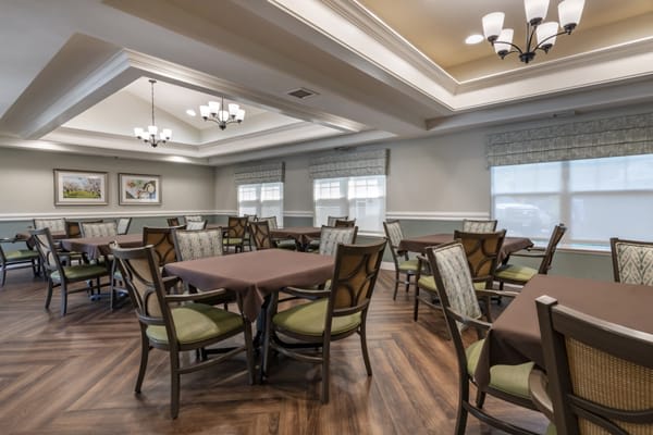 A well-lit dining room with multiple tables and chairs, featuring elegant light fixtures and wooden flooring.