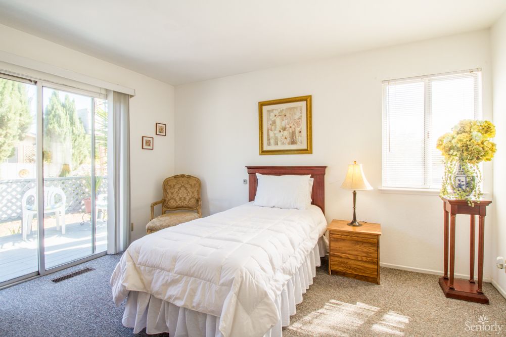 A bright bedroom with minimalist decor featuring a single bed, nightstand, and armchair.