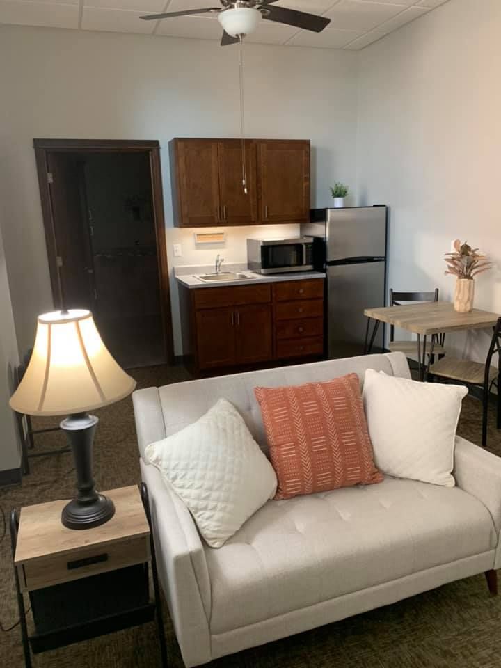 Cozy living space with a sofa, lamp, and kitchenette featuring modern appliances.