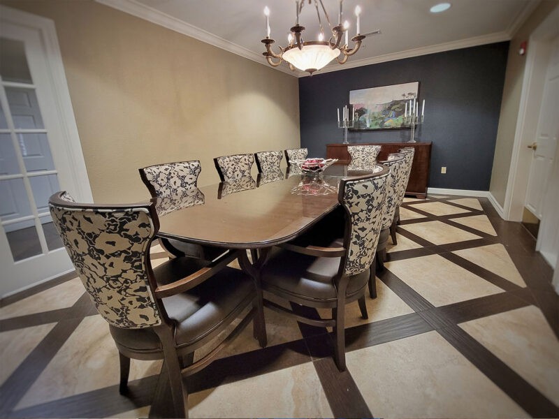 A sophisticated dining room featuring a large wooden table and patterned chairs, illuminated by an elegant chandelier.