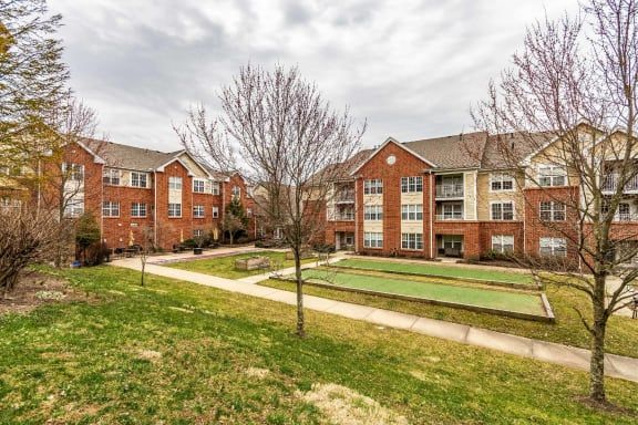 A residential apartment complex with a brick exterior, surrounded by trees and a neatly manicured lawn.
