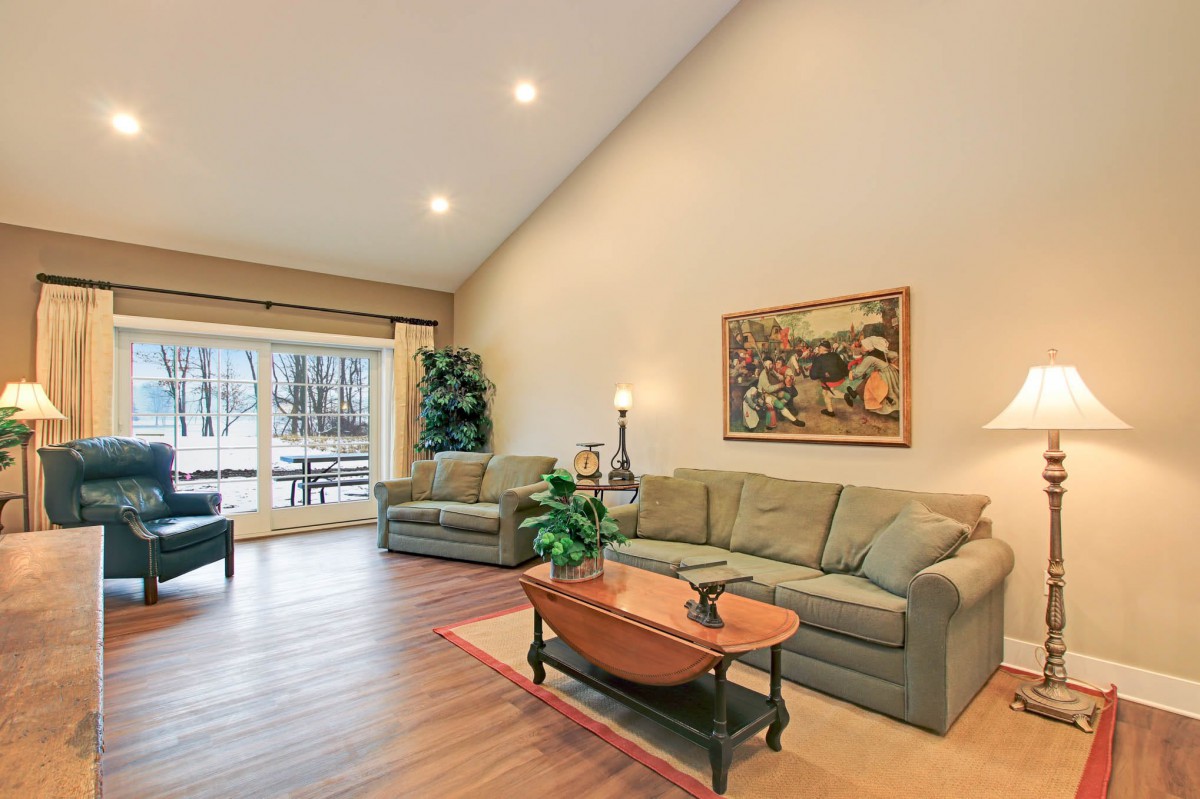 A spacious living room with high ceilings, featuring comfortable sofas, a wooden coffee table, artwork on the walls, and large windows overlooking a scenic view.