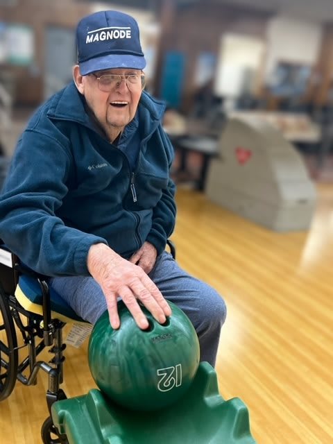 An elderly person in a wheelchair prepares to bowl at an indoor alley.