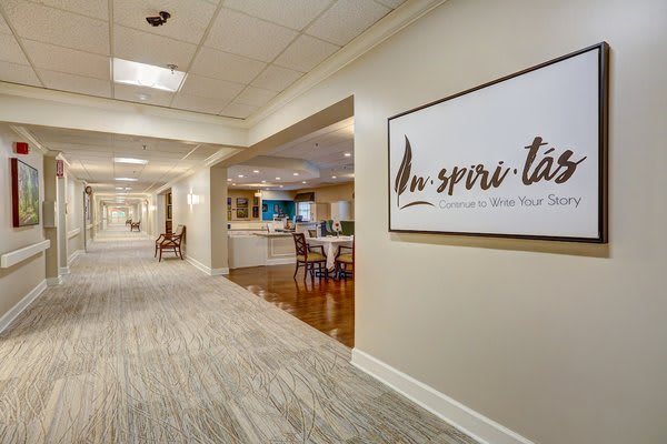 A well-lit hallway with a sign on the wall and a glimpse into a room furnished with chairs and tables.