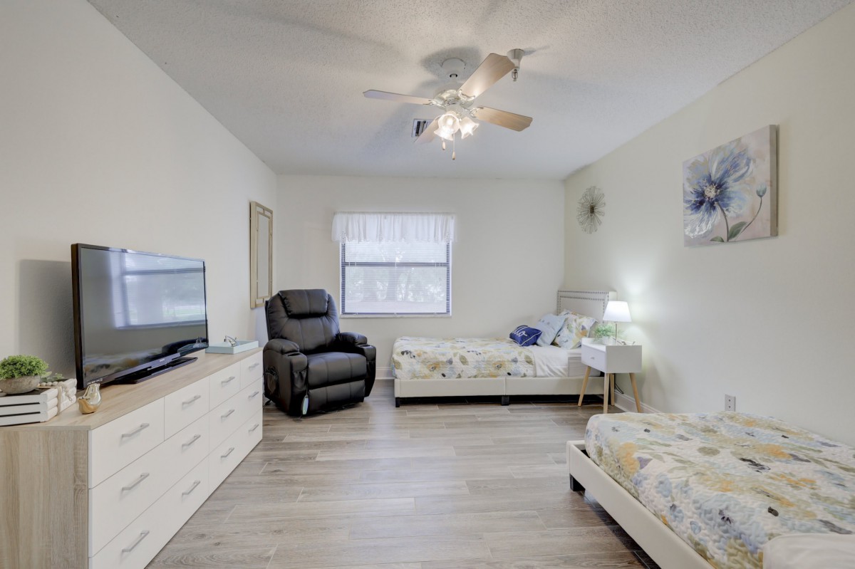 A cozy bedroom featuring two beds, a recliner, and a TV.