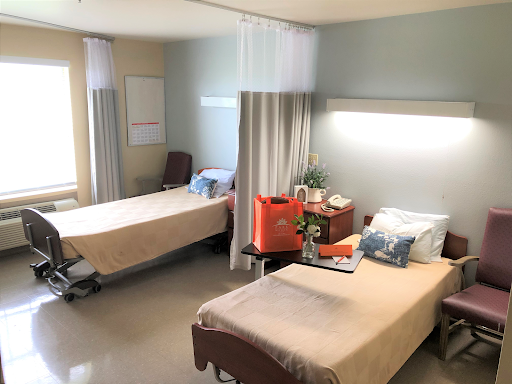 A view of a hospital patient room featuring two separate beds, curtains for privacy, and basic furnishings.