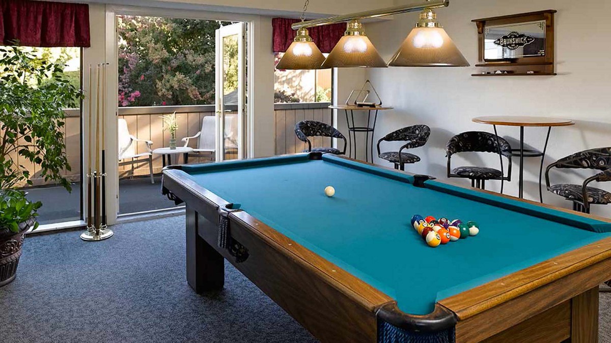 A cozy game room featuring a pool table, bar stools, and a view of the balcony through an open door.