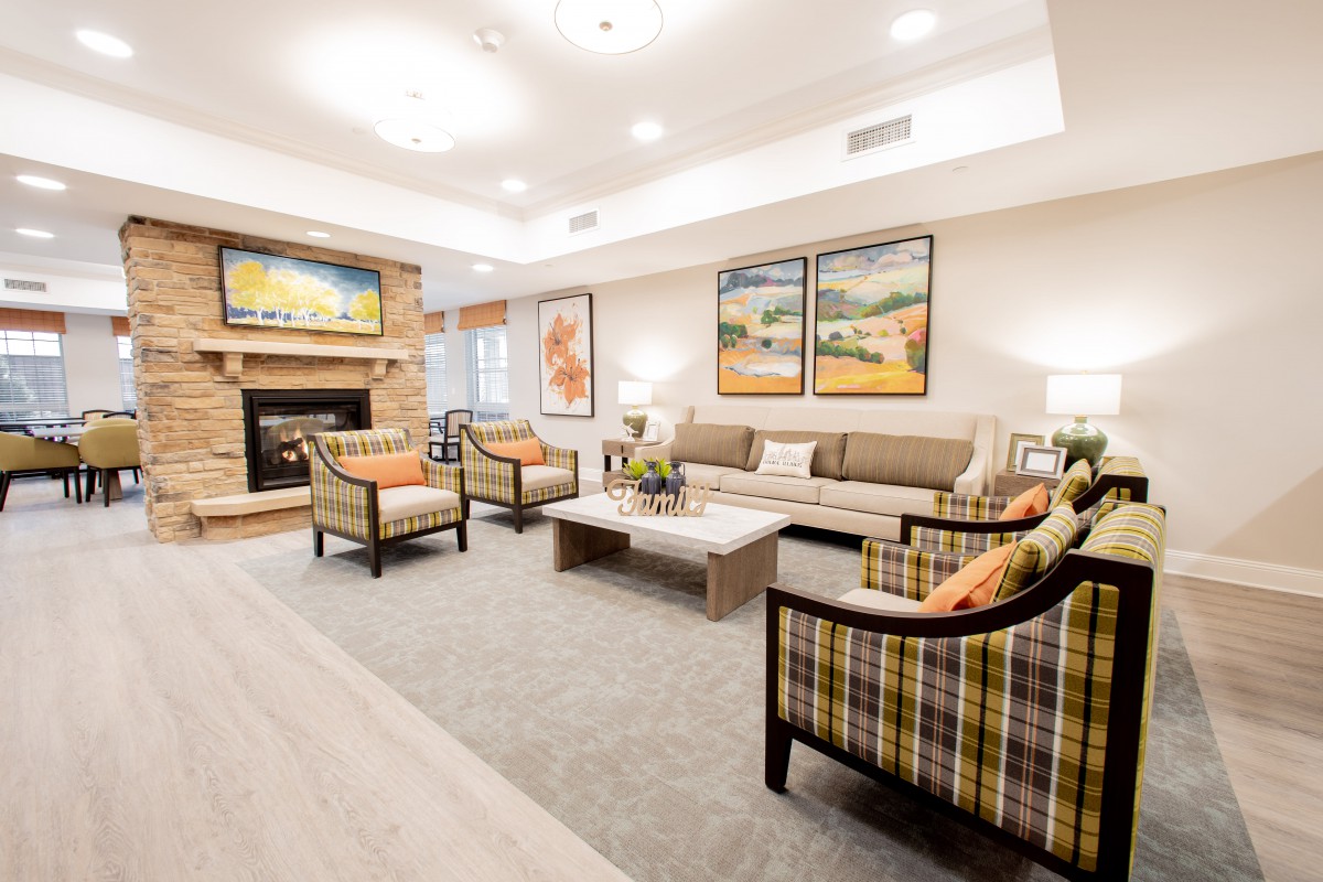 A cozy and elegantly decorated living room featuring a sofa, armchairs, and a fireplace with artwork on the walls.